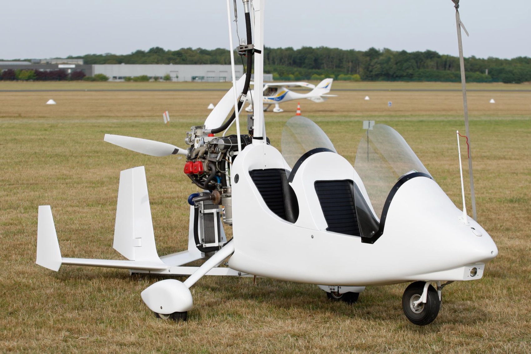 An open tandem gyrocopter parked with its Rotax engine and pusher propeller visible.