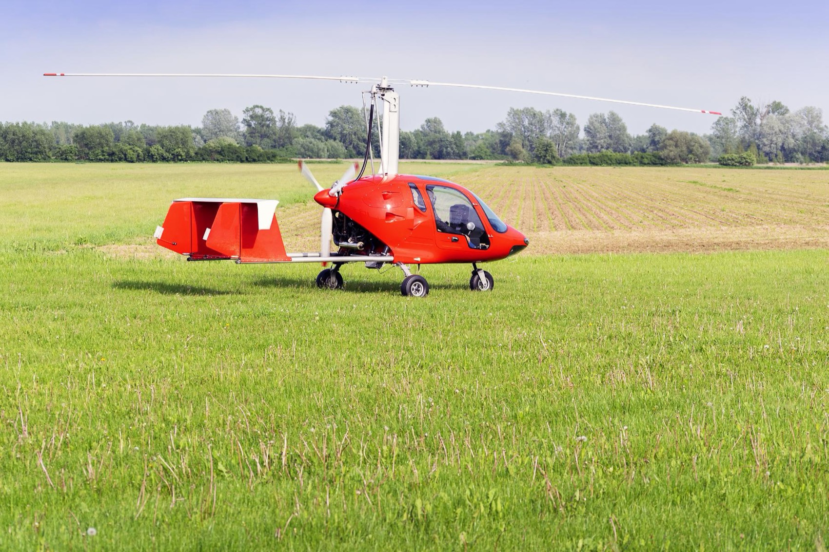 A red enclosed gyrocopter parked in a field, the kind of hull an owner insures.