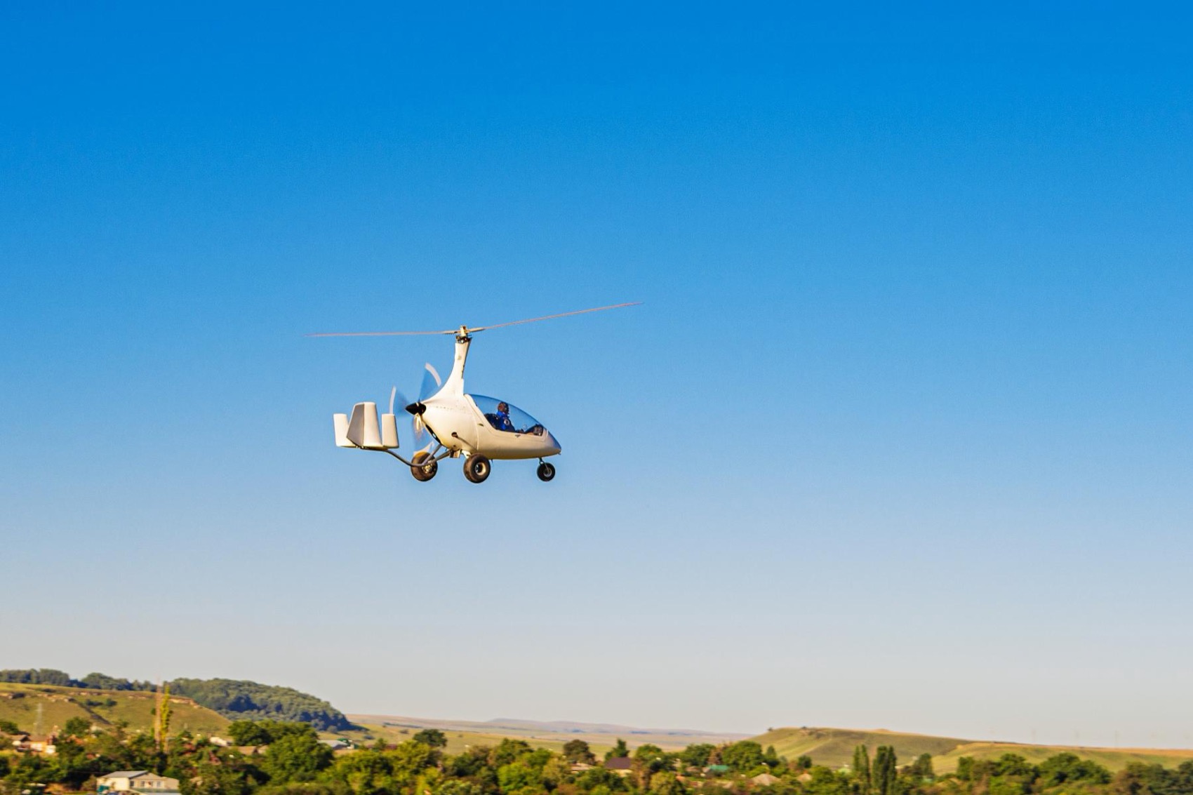 A piloted gyrocopter in flight over countryside, the crewed answer to the drone.
