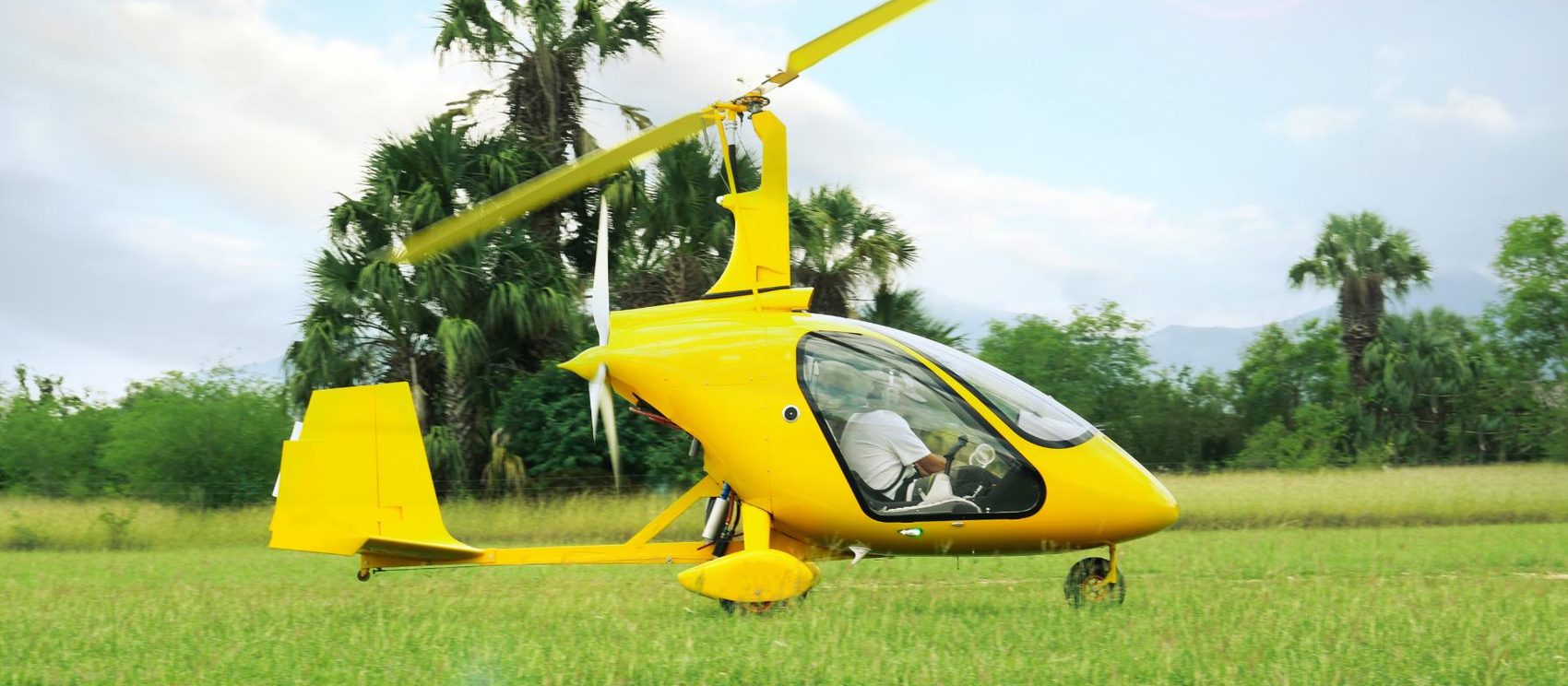 Yellow gyroplane on a grass strip with its rotor turning